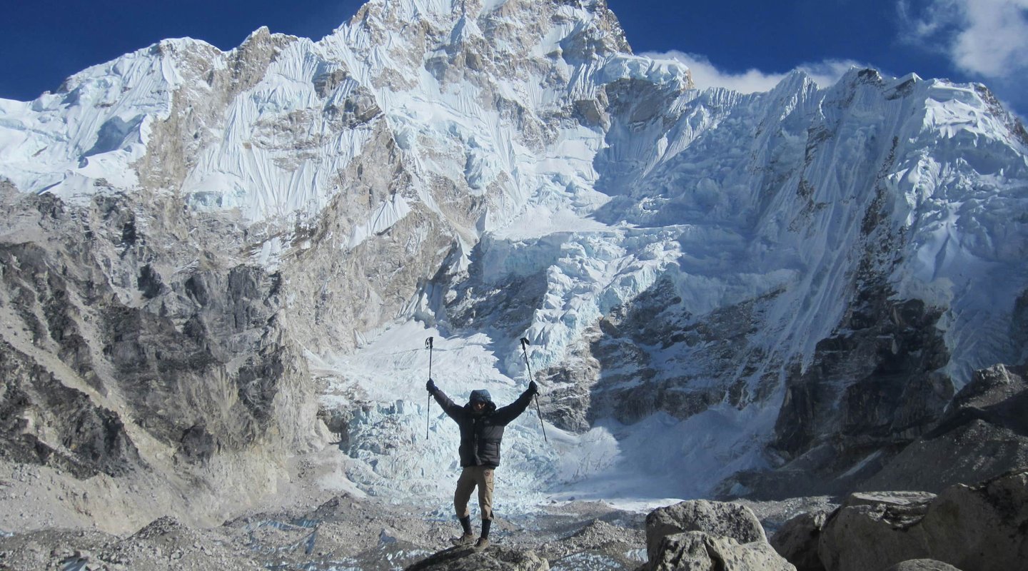 Trekker celebrating at the base of Mount Everest with panoramic view of snow-covered peaks and glaciers during the Gokyo Cho La Pass trek in Nepal Himalayas.