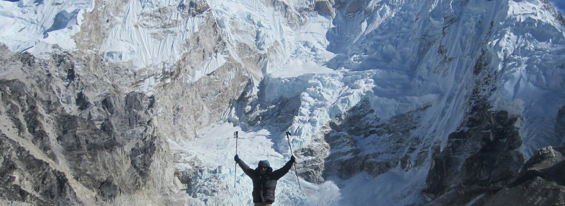 Trekker celebrating at the base of Mount Everest with panoramic view of snow-covered peaks and glaciers during the Gokyo Cho La Pass trek in Nepal Himalayas.