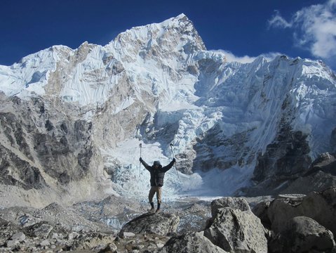 Trekker celebrating at the base of Mount Everest with panoramic view of snow-covered peaks and glaciers during the Gokyo Cho La Pass trek in Nepal Himalayas.