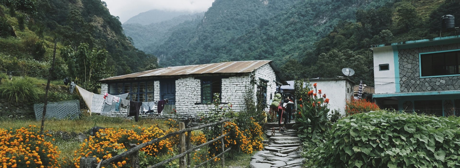Stone‑walled Himalayan tea house with outdoor tables and tent against misty mountain slopes