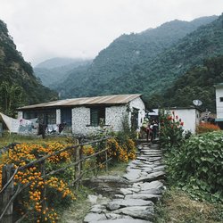 Stone‑walled Himalayan tea house with outdoor tables and tent against misty mountain slopes