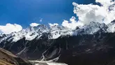 A group of hikers in colorful jackets walking single-file along a narrow, snow-covered ridge during the Langtang Valley Trek, with expansive snowy mountain slopes and distant peaks under a vibrant blue sky