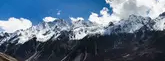 A group of hikers in colorful jackets walking single-file along a narrow, snow-covered ridge during the Langtang Valley Trek, with expansive snowy mountain slopes and distant peaks under a vibrant blue sky
