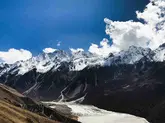 A group of hikers in colorful jackets walking single-file along a narrow, snow-covered ridge during the Langtang Valley Trek, with expansive snowy mountain slopes and distant peaks under a vibrant blue sky