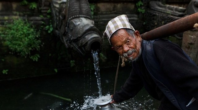 an-ond-man-collecting-water-from-a-traditional-tap-in-nepal