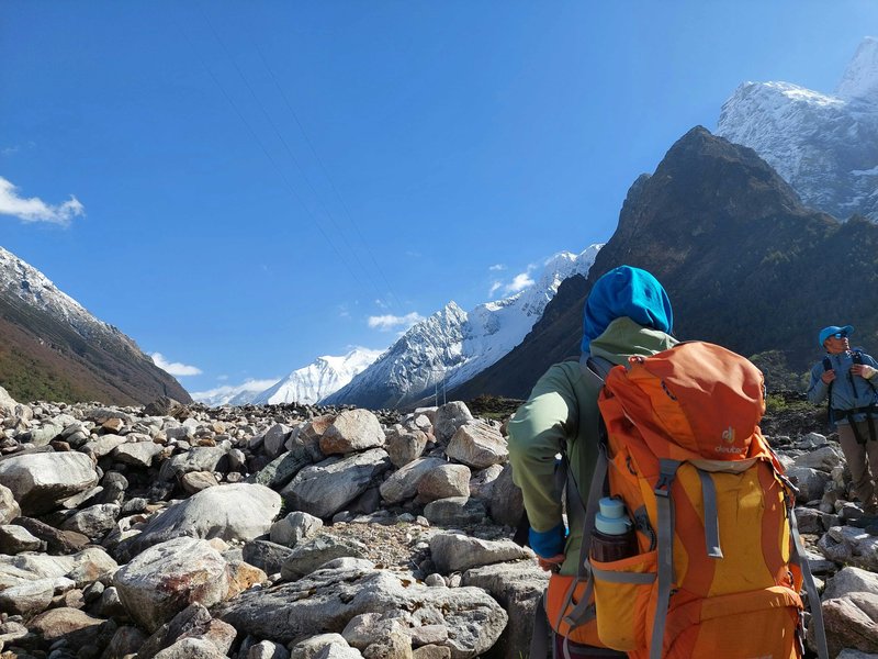 Trekkers with colorful backpacks crossing rocky glacier moraine approaching Annapurna Base Camp with Himalayan peaks in background