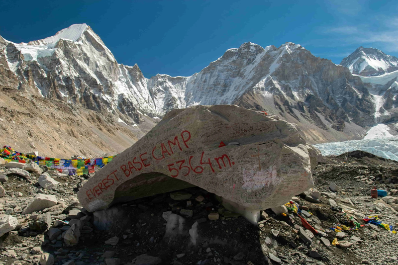 Stone marker at Everest Base Camp with inscription surrounded by rocks and Himalayan landscape