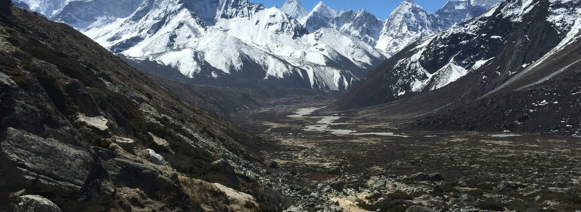 Trekkers walking along a rocky trail in the Everest region with snow-covered Himalayan peaks in the background during the Three Pass Trek in Nepal.