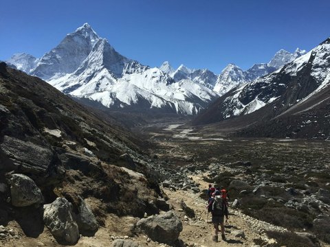 Trekkers walking along a rocky trail in the Everest region with snow-covered Himalayan peaks in the background during the Three Pass Trek in Nepal.