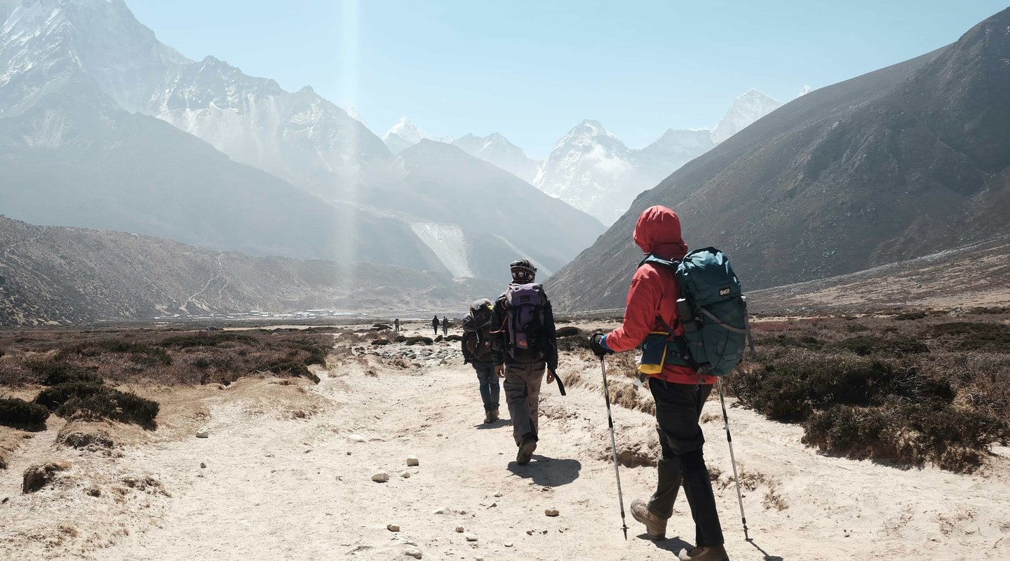 Group of trekkers hiking on a rugged trail with backpacks and trekking poles during the Everest Three Pass trek in Nepal, surrounded by Himalayan peaks.