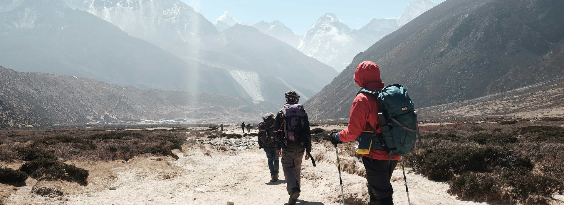 Group of trekkers hiking on a rugged trail with backpacks and trekking poles during the Everest Three Pass trek in Nepal, surrounded by Himalayan peaks.