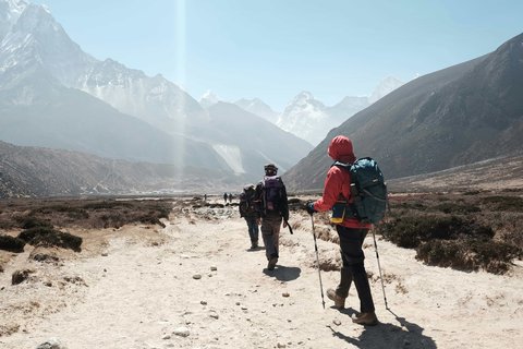 Group of trekkers hiking on a rugged trail with backpacks and trekking poles during the Everest Three Pass trek in Nepal, surrounded by Himalayan peaks.