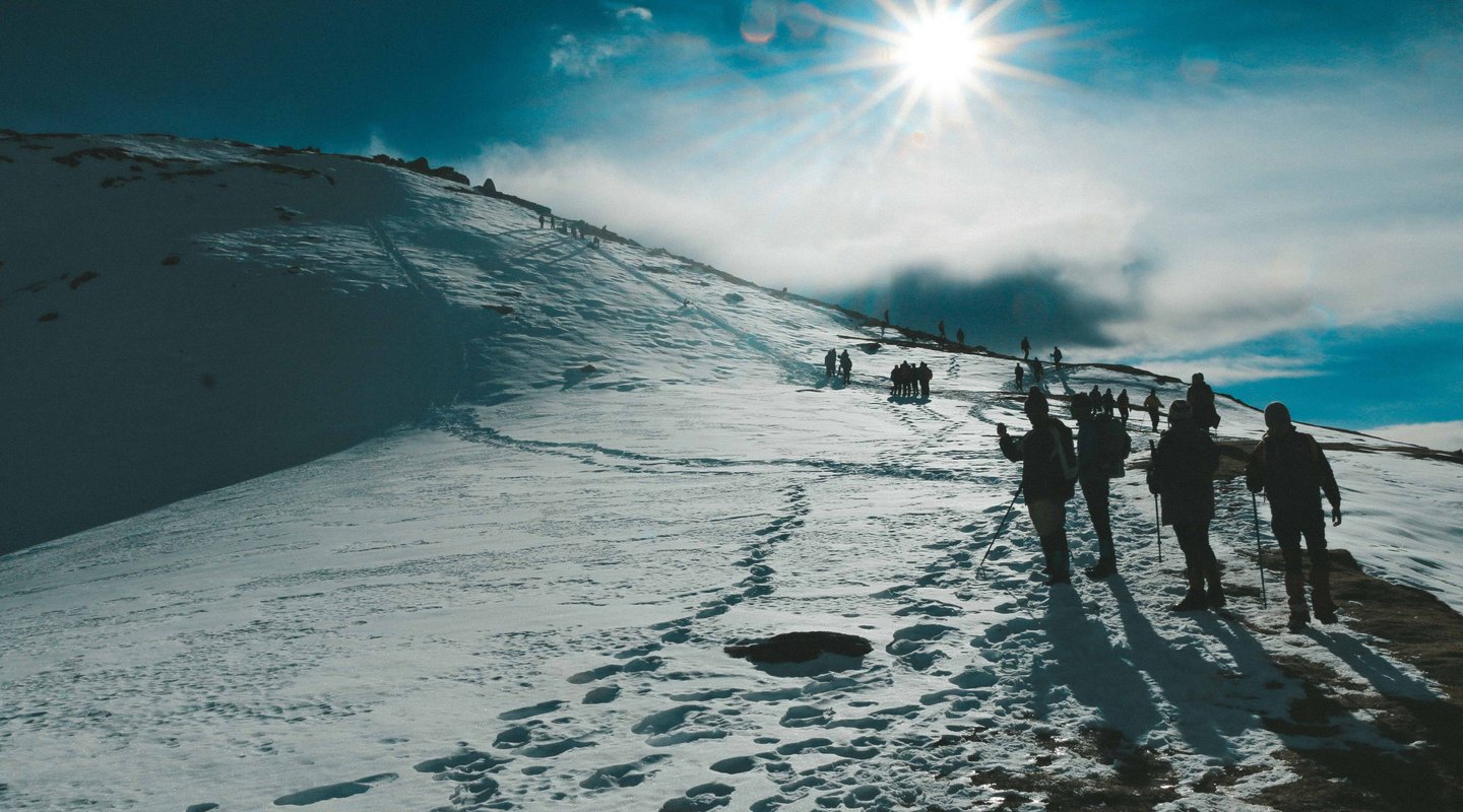 Trekkers hiking on a snow-covered trail under bright sunlight on the Gokyo Cho La Pass trek in Nepal