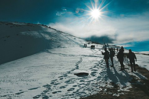 Trekkers hiking on a snow-covered trail under bright sunlight on the Gokyo Cho La Pass trek in Nepal