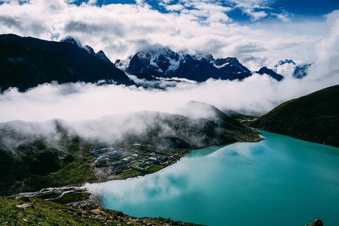 Scenic view of Gokyo Lake with turquoise waters, Himalayan peaks, and Gokyo village surrounded by clouds in the Everest region of Nepal.