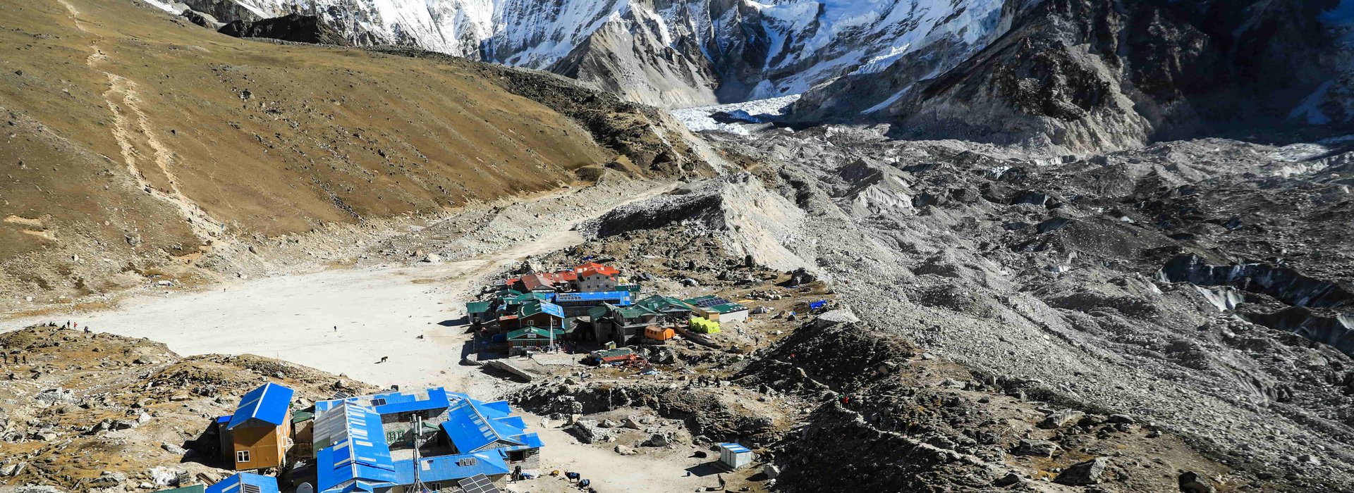 A panoramic view of Gorak Shep village along the Everest Base Camp trek route, with snow-capped Himalayan peaks and glaciers in the background under a clear blue sky