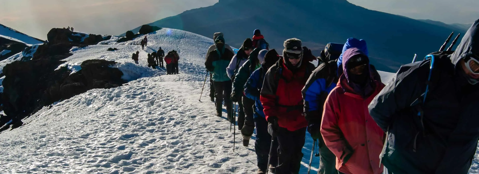 People hiking up Mount Kilimanjaro on a steep trail with rocky terrain and high-altitude landscape