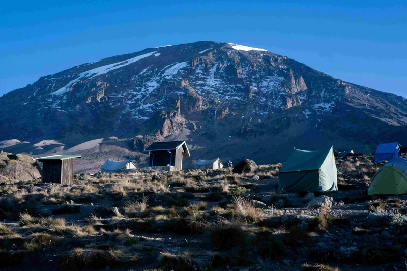 Small camping tent set up at the base of Mount Kilimanjaro with mountain slopes in the background