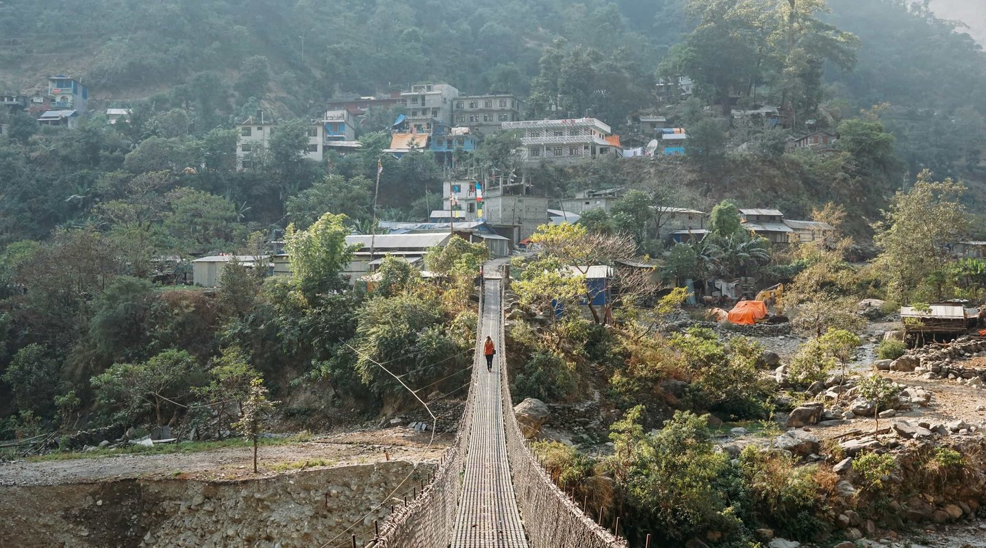 Suspension bridge leading to Samagaun village on the Manaslu Circuit Trek, surrounded by traditional stone houses and towering Himalayan peaks.