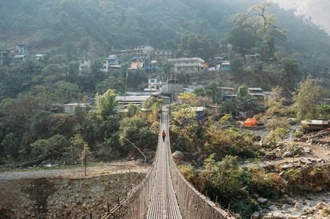 Suspension bridge leading to Samagaun village on the Manaslu Circuit Trek, surrounded by traditional stone houses and towering Himalayan peaks.