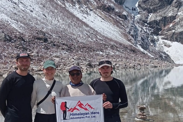 Group of trekkers celebrating at Larkya La Pass on the Manaslu Circuit Trek with colorful prayer flags and snow-covered Himalayan peaks in the background.