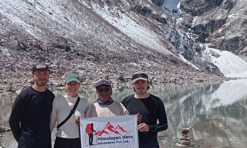 Group of trekkers celebrating at Larkya La Pass on the Manaslu Circuit Trek with colorful prayer flags and snow-covered Himalayan peaks in the background.