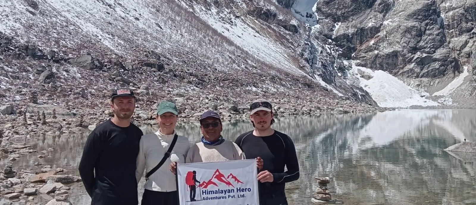 Group of trekkers celebrating at Larkya La Pass on the Manaslu Circuit Trek with colorful prayer flags and snow-covered Himalayan peaks in the background.