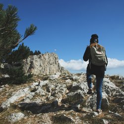 “Woman trekking along a rocky talus path of Manaslu region with snow-capped peaks rising in the distance.”