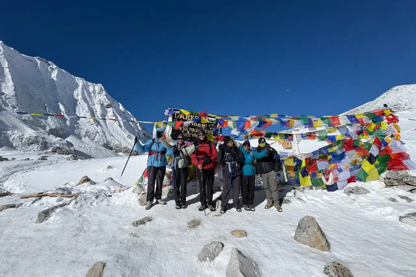 Group of trekkers celebrating at Larkya La Pass on the Manaslu Circuit Trek with colorful prayer flags and snow-covered Himalayan peaks in the background.