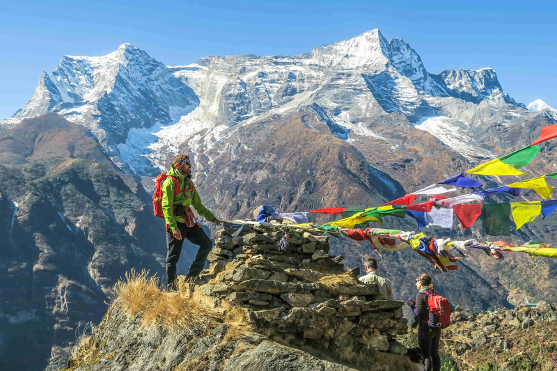Trekker walking toward Everest Base Camp with snowy mountains in the background and colorful prayer flags along the trail