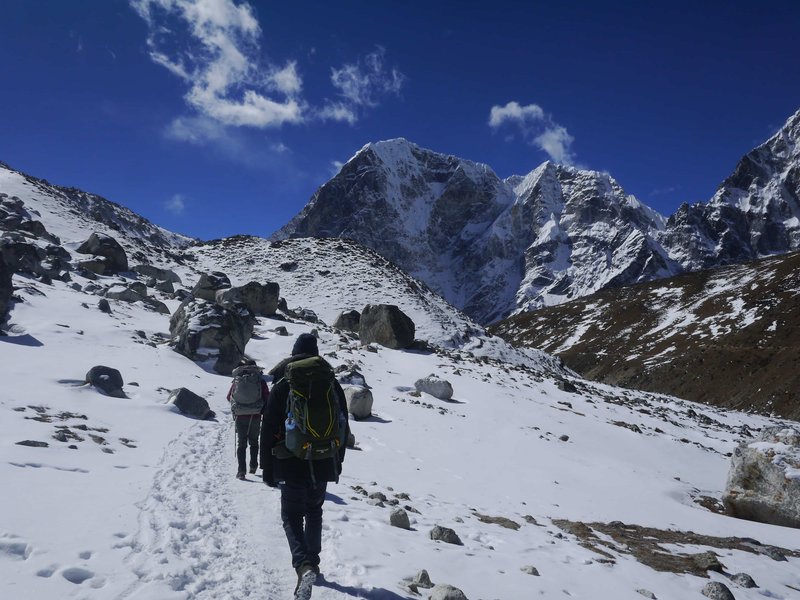 Group of trekkers following snowy footpath toward Annapurna Base Camp with dramatic mountain walls and clear blue sky
