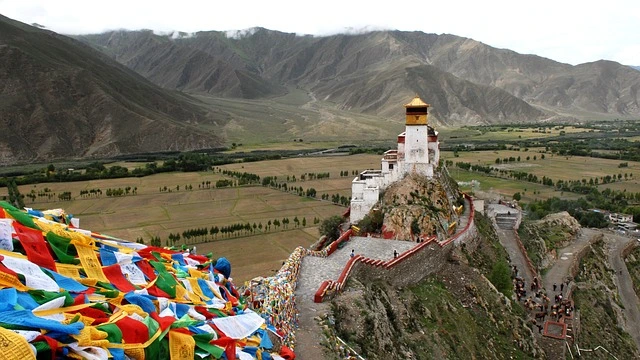 Tibetan monastery overlooking vast Tibet landscapes with colorful prayer flags and Himalayan valleys in the distance.